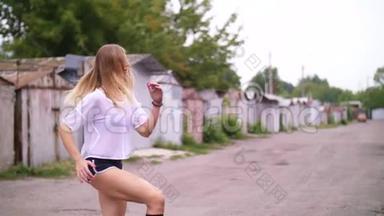 运动的年轻金发女人穿短裤，在轮胎的帮助下进行各种力量练习，跳跃。 在夏天